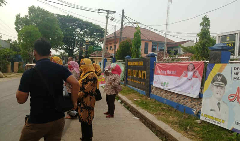 Kades Bumi bakti bagi-bagi masker di pinggir jalan desa.