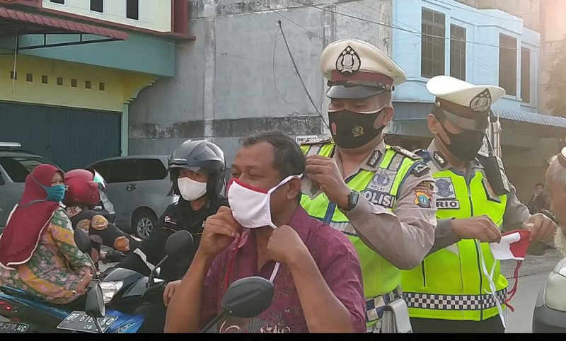 Seorang polantas di Karimun memasangkan masker kepada seorang pengendara. Polisi Kawal Penerapan Sanksi bagi Pelanggar Protokol Kesehatan di Karimun. (Foto: yra)