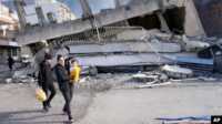 gempa di Turki Seorang perempuan menggendong bayi melewati bangunan yang hancur di Kota Iskenderun, Turki selatan, Selasa, 7 Februari 2023. (Foto: AP via VOA)
