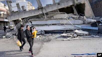 gempa di Turki Seorang perempuan menggendong bayi melewati bangunan yang hancur di Kota Iskenderun, Turki selatan, Selasa, 7 Februari 2023. (Foto: AP via VOA)