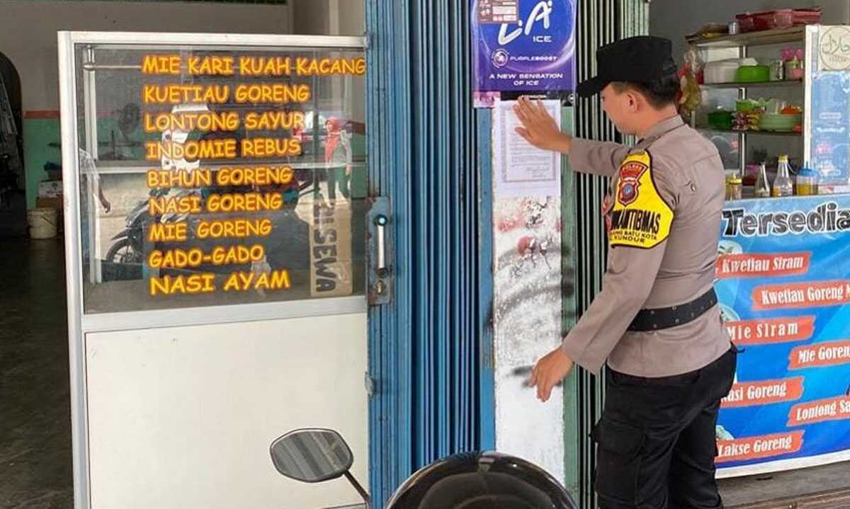 Seorang Bhabinkamtibmas menempelkan brosur maklumat larangan bakar hutan dan lahan di salah satu warung makan di Tanjung Balai Karimun,, Rabu (17/5/2023). (Dok. Humas Polres Karimun)