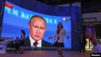Vladimir Putin Peserta berkumpul di dekat layar yang memperlihatkan Presiden Rusia Vladimir Putin, yang menyampaikan pidato di Forum Ekonomi Internasional St. Petersburg (SPIEF) di Saint Petersburg, Rusia, 17 Juni 2022. (Foto: REUTERS/Anton Vaganov)