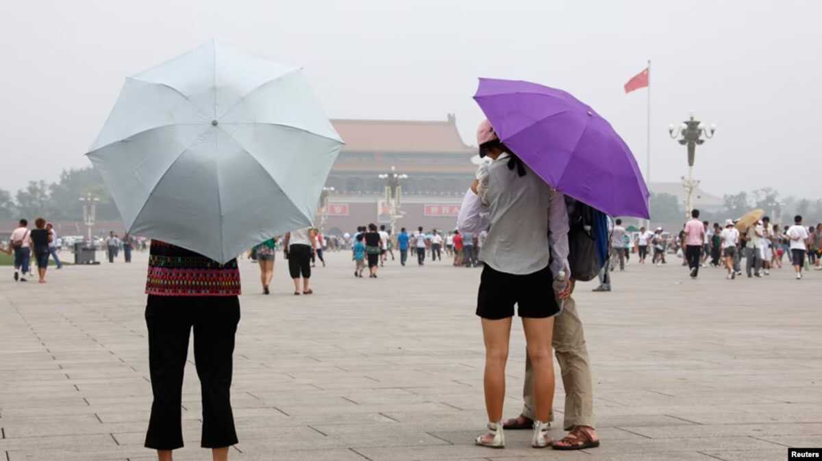 Pengunjung ke Lapangan Tiananmen melindungi diri dari matahari dengan payung di hari yang panas dan berkabut di Beijing. (Foto: Reuters via VOA)