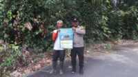 sosialisasi PMK bhabinkamtibmas karimun Bhabinkamtibmas Kelurahan Darussalam, Kecamatan Meral, Aipda Samson Tarigan berpose bersama warga sambil menunjukkan poster imbauan pencegahan penyakit mulut dan kuku (PMK) pada hewan ternak, Selasa (1/8/2023). (Dok. Humas Polres Karimun)