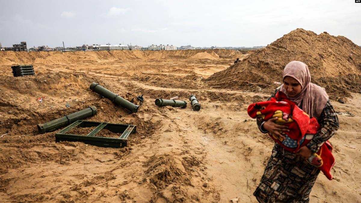 Seorang warga Palestina menggendong bayi berjalan melewati kontainer amunisi yang ditinggalkan oleh pasukan Israel saat dia melarikan diri lebih jauh ke selatan dari Khan Yunis di Jalur Gaza selatan, 2 Februari 2024. (Mahmud Hams/AFP)