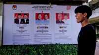Seorang pria berjalan melewati spanduk KPU yang memperlihatkan foto-foto calon presiden di Jakarta, 22 Januari 2024. Indonesia dijadwalkan mengadakan pemilihan presiden pada 14 Februari. (AP/Dita Alangkara)