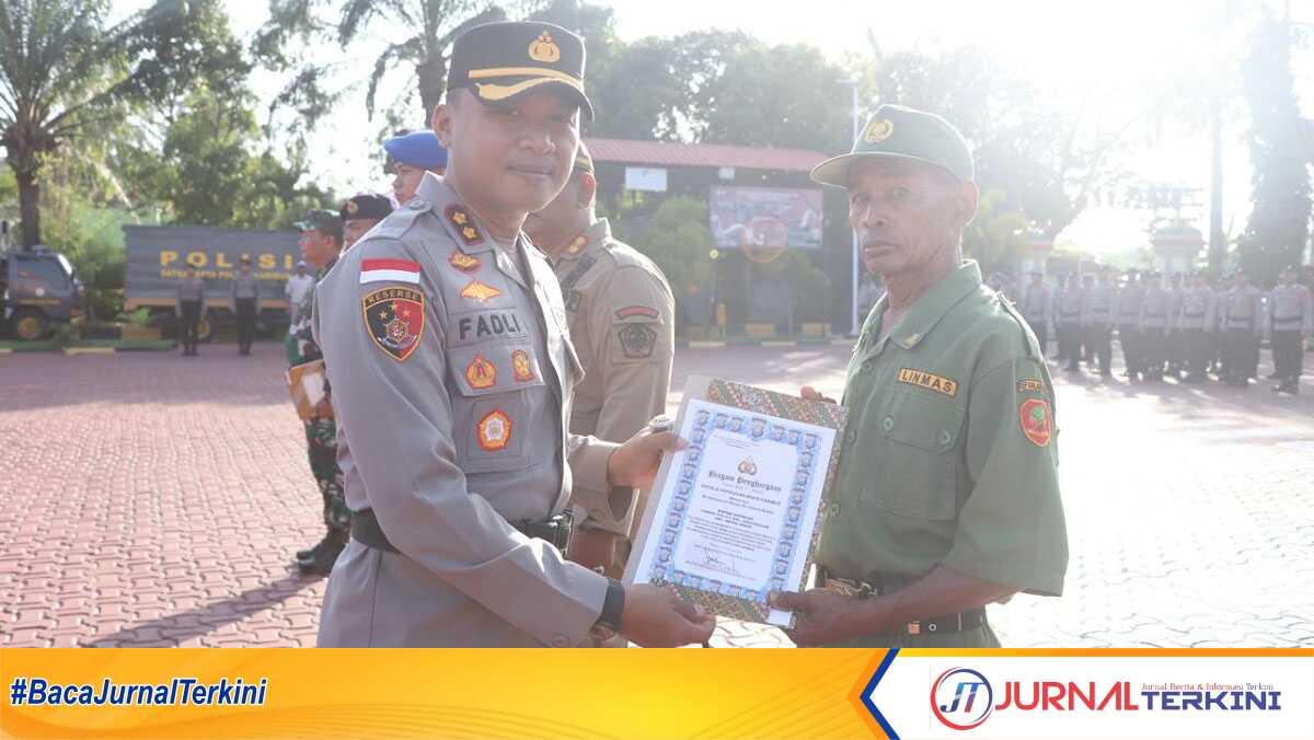 Kapolres Karimun AKBP Fadli Agus memberikan penghargaan kepada Supriadi, anggota Linmas yang bertugas membantu pengamanan Pemilu di TPS 11 Kelurahan Darussalam, Kecamatan Meral Barat. Penghargaan diberikan dalam upacara Hari Kesadaran Nasional di Mapolres Karimun, Selasa (19/2/2024). (jurnalterkini.id/jansen)