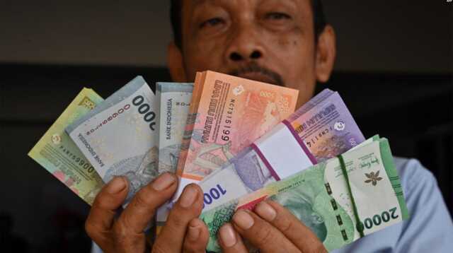 Seorang pria memperlihatkan uang kertas Rupiah baru yang akan diberikan kepada anggota keluarganya selama perayaan Idulfitri pada 28 Maret 2024. (Foto: AFP)
