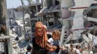 perempuan palestina mengungsi Seorang perempuan Palestina menggendong putrinya saat berjalan melewati puing-puing rumah yang hancur akibat serangan militer Israel, di Khan Younis di selatan Jalur Gaza, 10 Juli 2024. (REUTERS/Hatem Khaled)