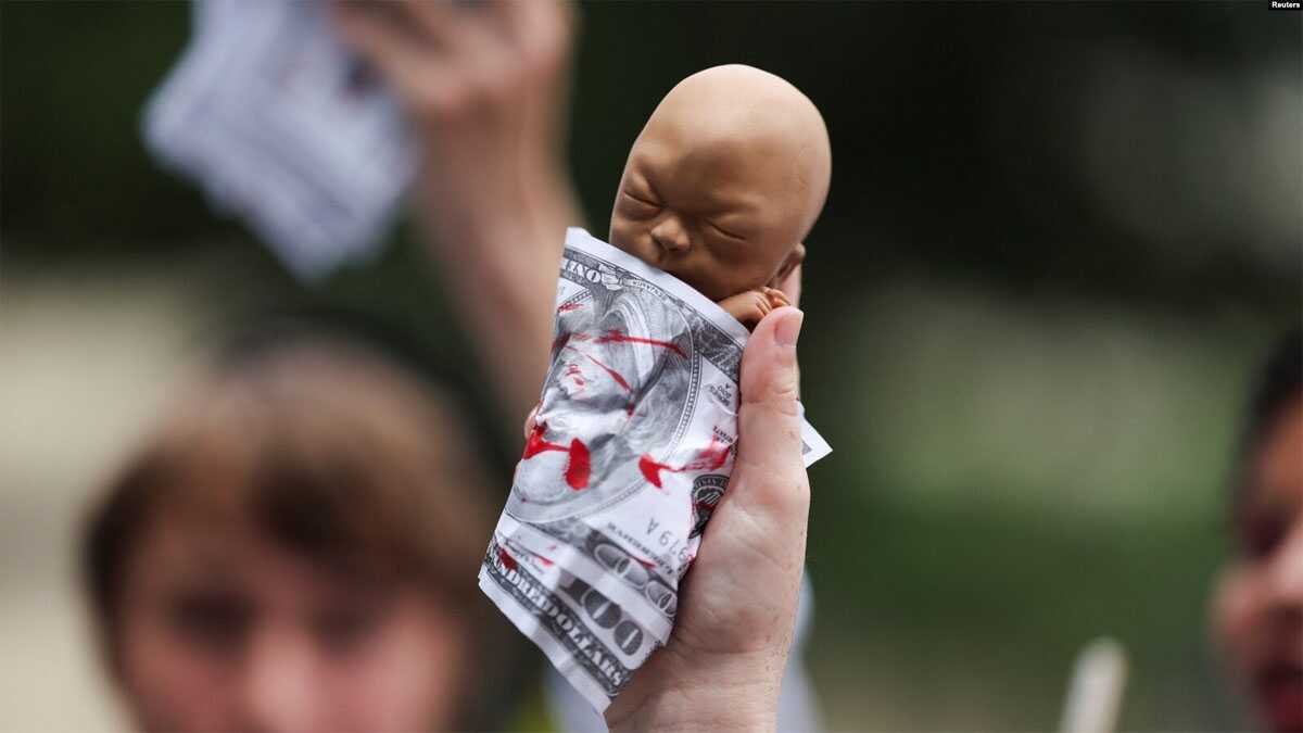 Seorang pegiat antiaborsi mengangkat alat peraga yang menggambarkan janin yang dibungkus dengan uang seratus dolar palsu di Milwaukee, Wisconsin, AS, 15 Juli 2024, sebagai ilustrasi. (Foto: REUTERS/Shannon Stapleton)