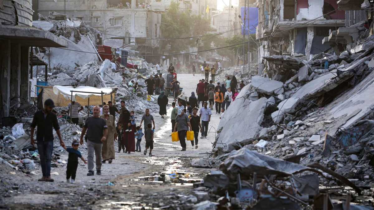 Warga Palestina yang mengungsi akibat serangan udara dan darat Israel di Jalur Gaza, berjalan melewati aliran limbah gelap yang mengalir ke jalan-jalan kota selatan Khan Younis, Jalur Gaza, pada 4 Juli 2024. (Foto: AP)