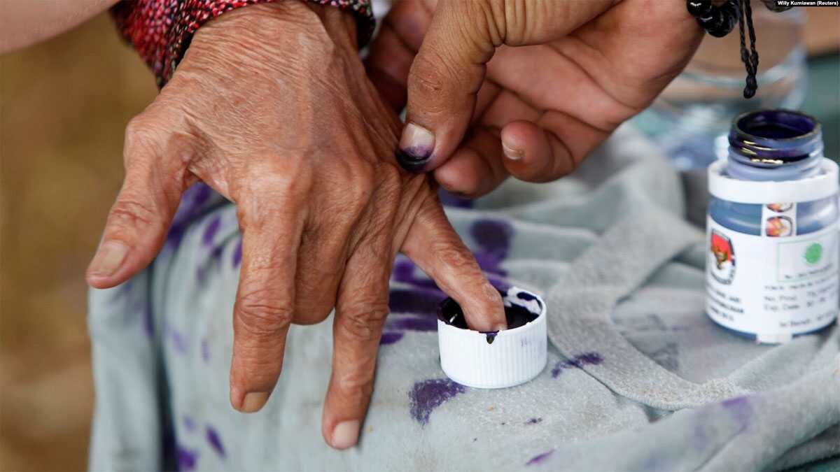 FILE - Seorang petugas pemilu membantu seorang perempuan lanjut usia untuk menandai jarinya dengan tinta setelah memberikan suaranya pada Pilkada di Tangerang, Banten, 27 Juni 2018. (Willy Kurniawan/REUTERS)