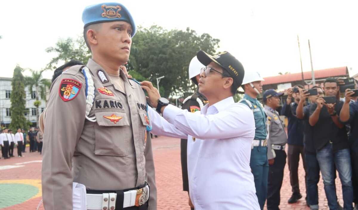 operasi lilin seligi Polres Karimun Bupati Karimun, Iskandarsyah menyematkan pita kepada salah satu personel yang terlibat dalam Operasi Lilin Seligi 2025 saat memimpin apel pasukan di Mapolres Karimun pada Jumat (19/12/2025). (Humas Polres Karimun)