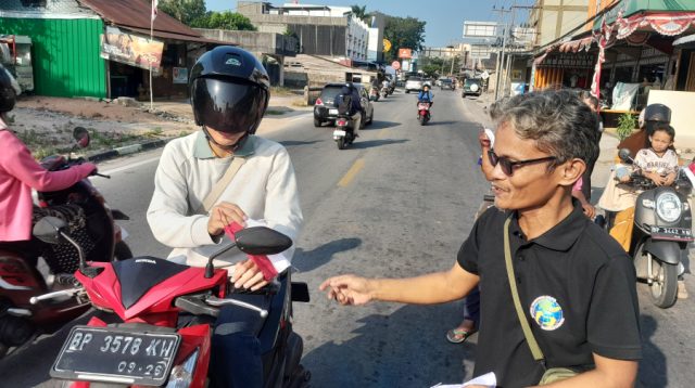 Ketua Ikatan Wartawan Online (IWO) Karimun membagikan bendera kepada seorang pengendara sepeda motor dalam HUT RI ke-81 yang disejalankan dengan HUT IWO ke-14 di simpang lampu merah Baran, Sabtu (15/8/2026). (Dokumentasi pribadi)