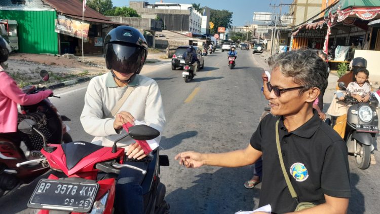 Ketua Ikatan Wartawan Online (IWO) Karimun membagikan bendera kepada seorang pengendara sepeda motor dalam HUT RI ke-81 yang disejalankan dengan HUT IWO ke-14 di simpang lampu merah Baran, Sabtu (15/8/2026). (Dokumentasi pribadi)